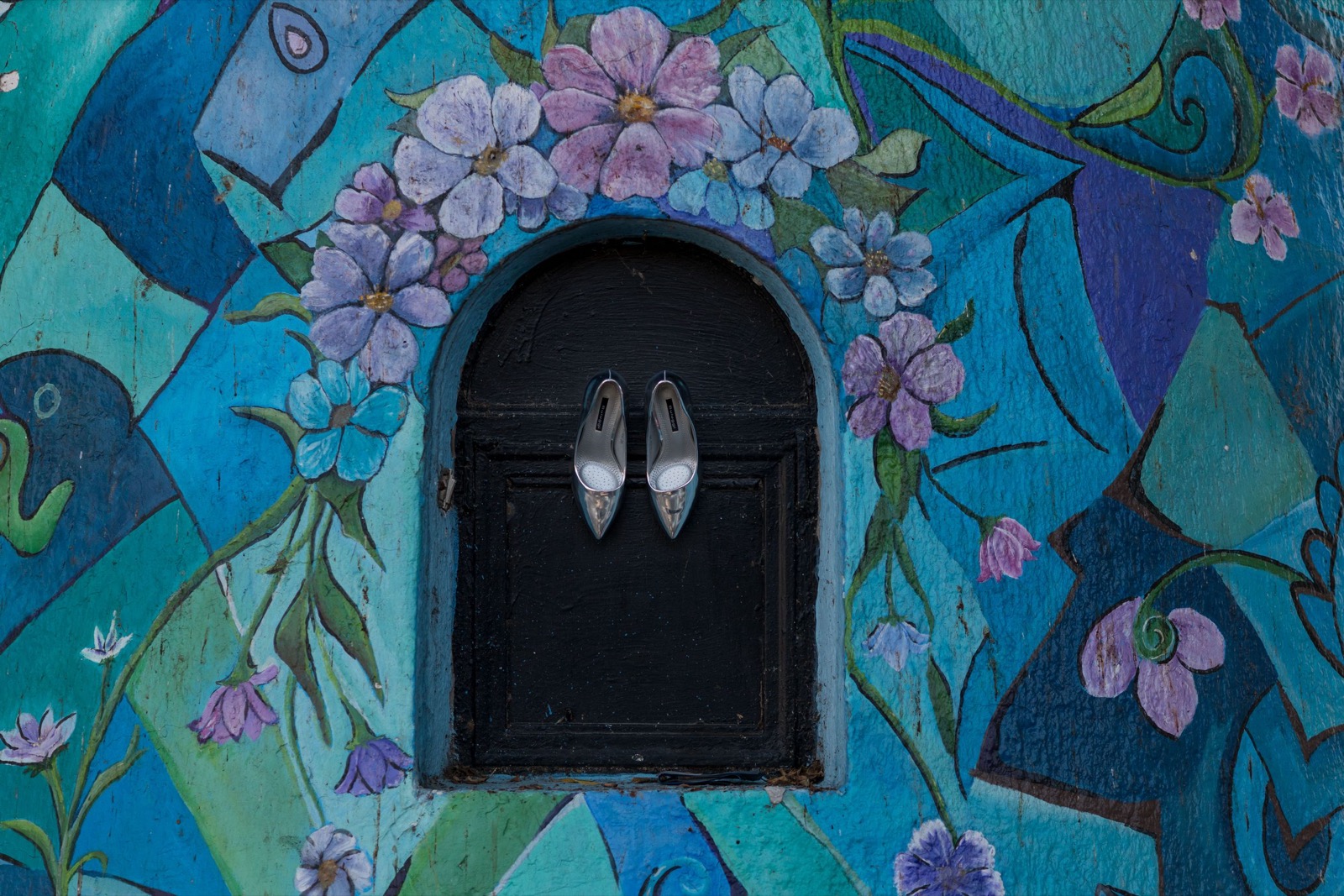 Zapatos de novia sobre una puerta enmarcada por un muro pintado con flores