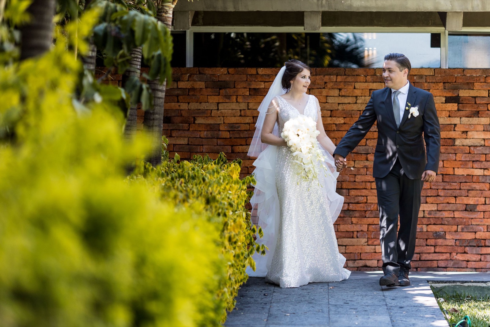 Los novios caminan de la mano por un jardín