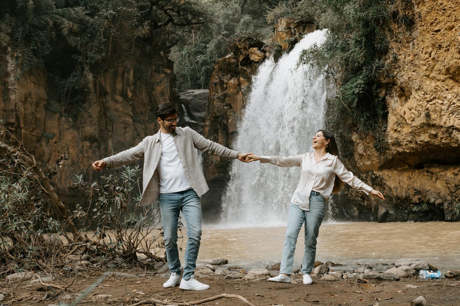 La pareja tomada de la mano frente a una cascada