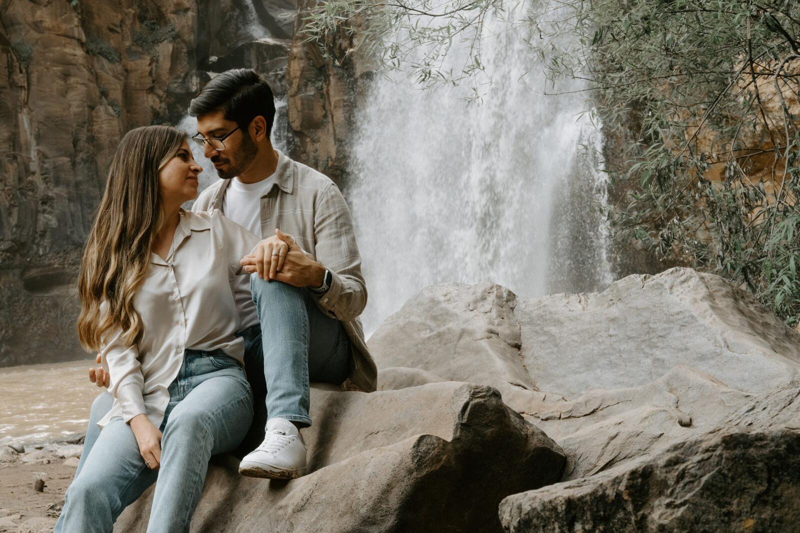 La pareja sentada en una roca junto a la cascada