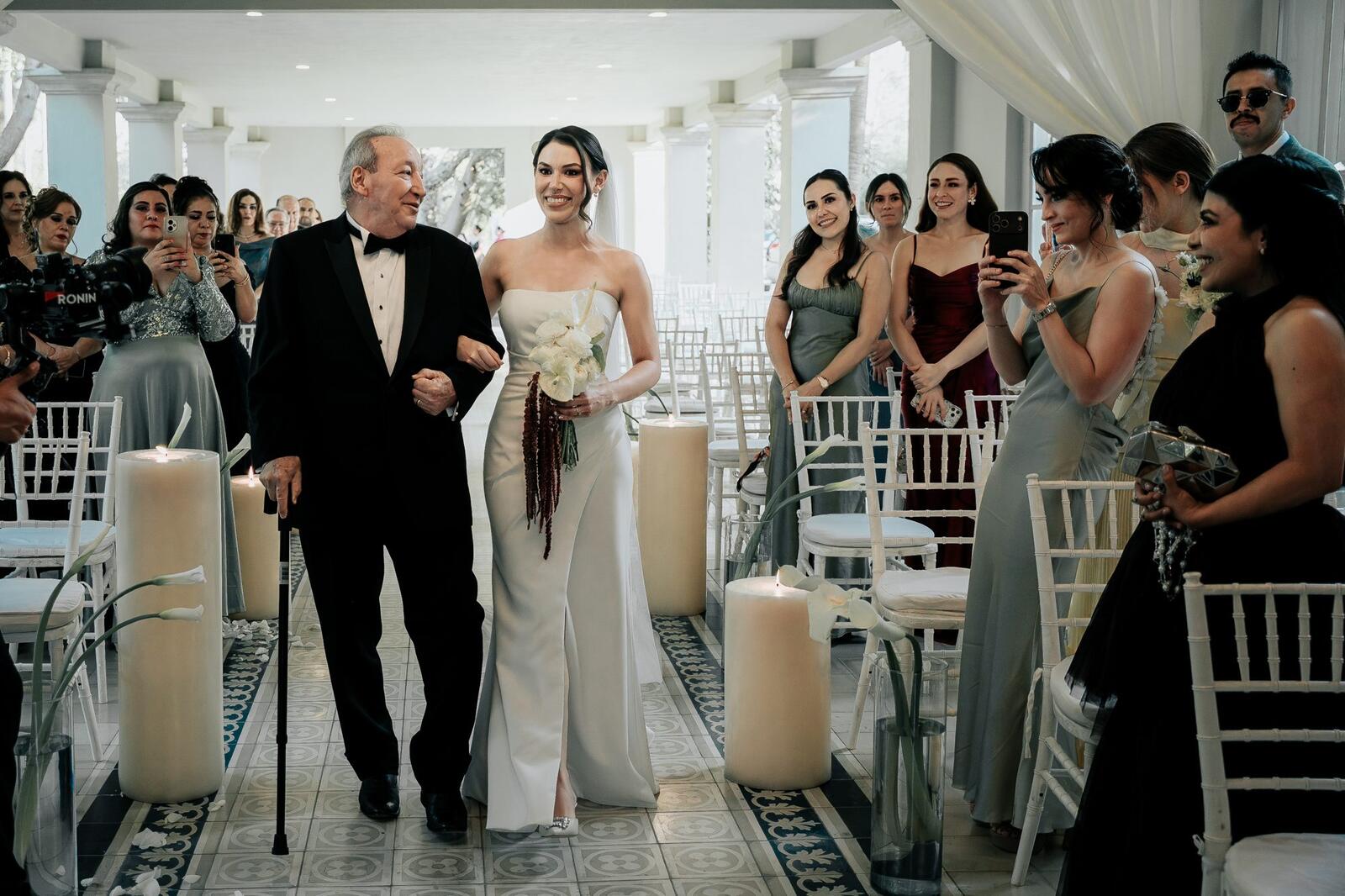 La novia entra a la ceremonia del brazo de su papá entre velas e invitados