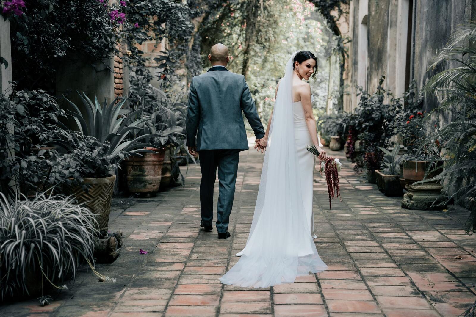 Los novios caminan por un pasillo de piedra rodeado de plantas
