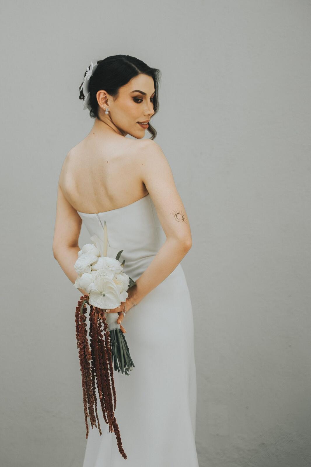 Retrato de la novia con vestido strapless y ramo de flores en tonos vino