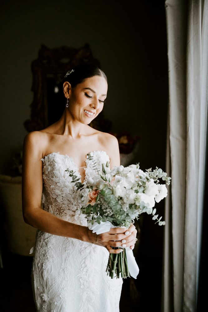 Novia con su ramo junto a una cortina oscura