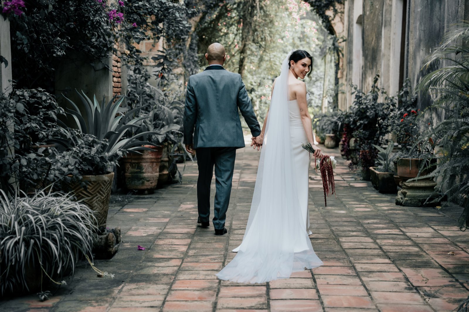 Los novios caminan de la mano por un pasillo con plantas