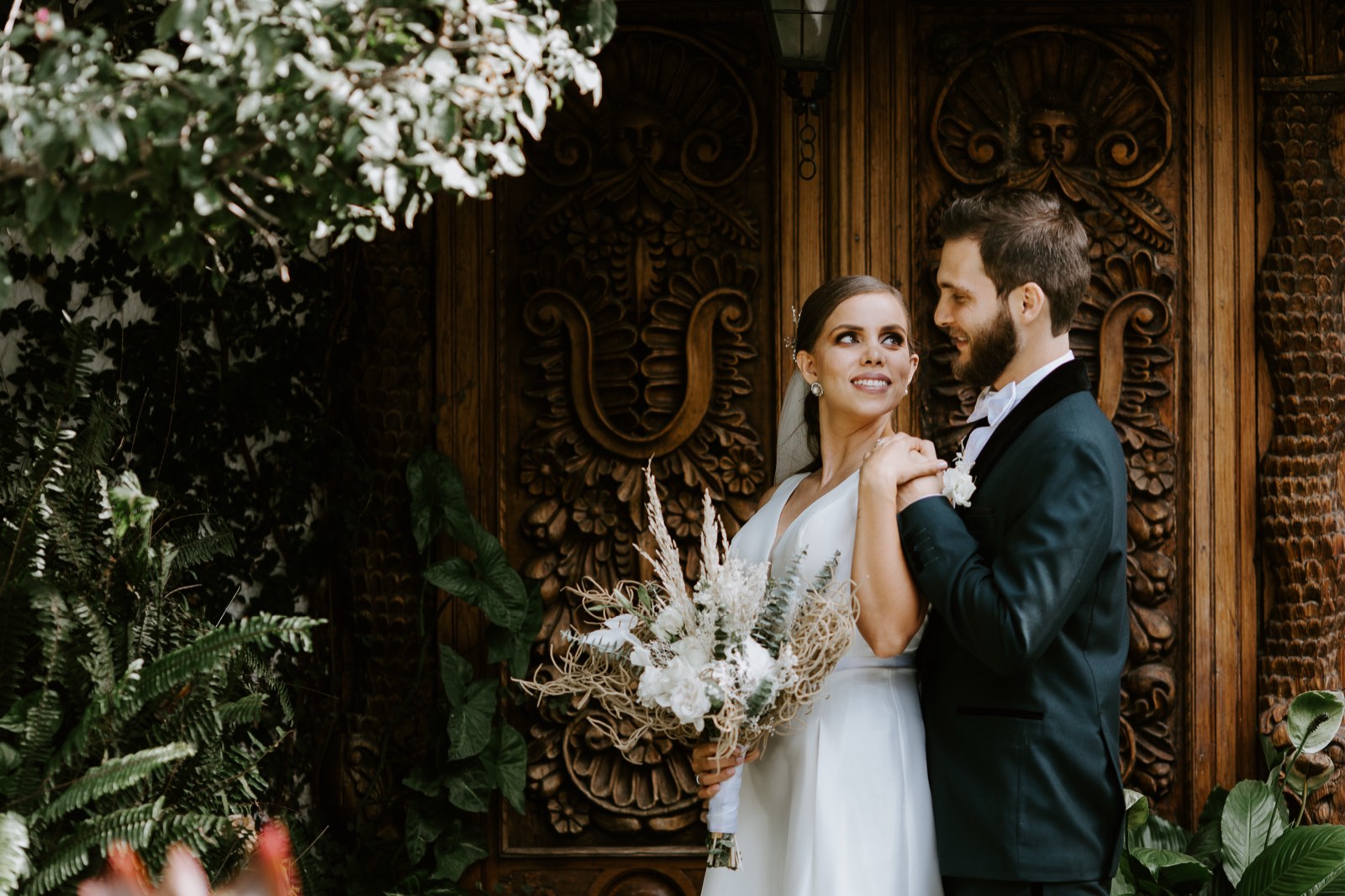 La novia sonríe al novio junto a una puerta de madera tallada
